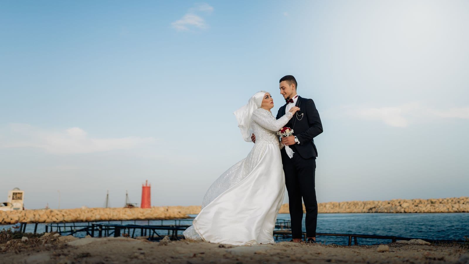 A couple standing together on a stone pier above the sea